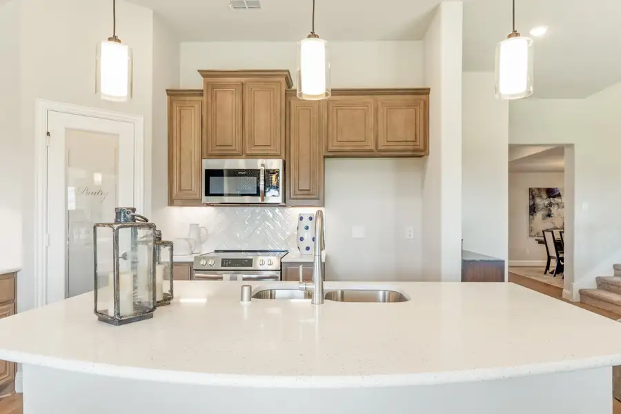 Kitchen with curved white quartz island, tan wood cabinets, herringbone tile backsplash, and three pendant lights