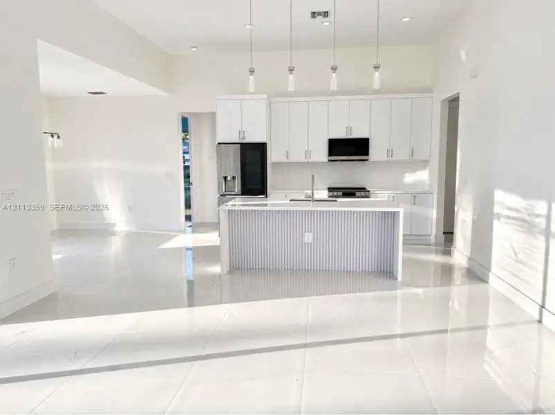 Kitchen featuring white cabinetry, an island with vertical slat detailing, polished tile flooring, stainless steel appliances, and four glass pendant lights