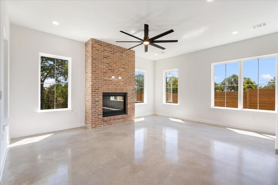 Unfurnished living room featuring plenty of natural light, a brick fireplace, finished concrete flooring, a ceiling fan, and recessed lighting
