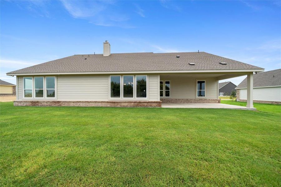 Back of house featuring brick siding, a patio, a lawn, a chimney, and roof with shingles