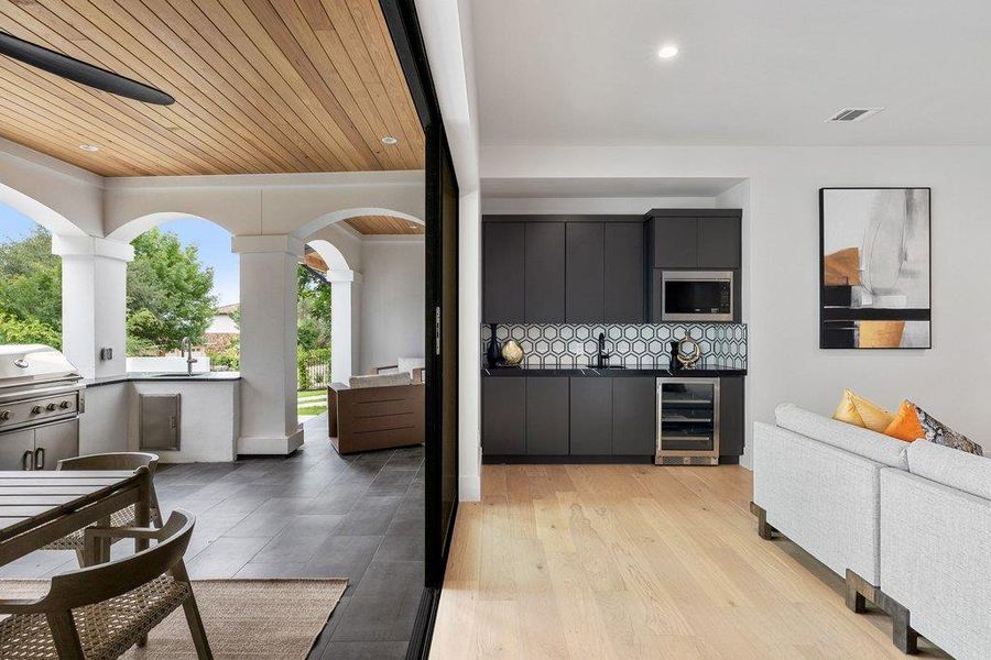Expansive outdoor living area featuring a wood-panel ceiling, dark tile flooring, and an integrated outdoor kitchen