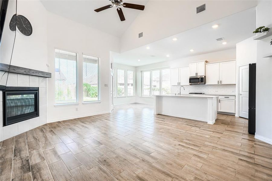 Unfurnished living room featuring high vaulted ceiling, a tile fireplace, light wood-style floors, ceiling fan, and recessed lighting Unfurnished living room featuring high vaulted ceiling, a tile fireplace, light wood-style floors, ceiling fan, and recessed lighting
