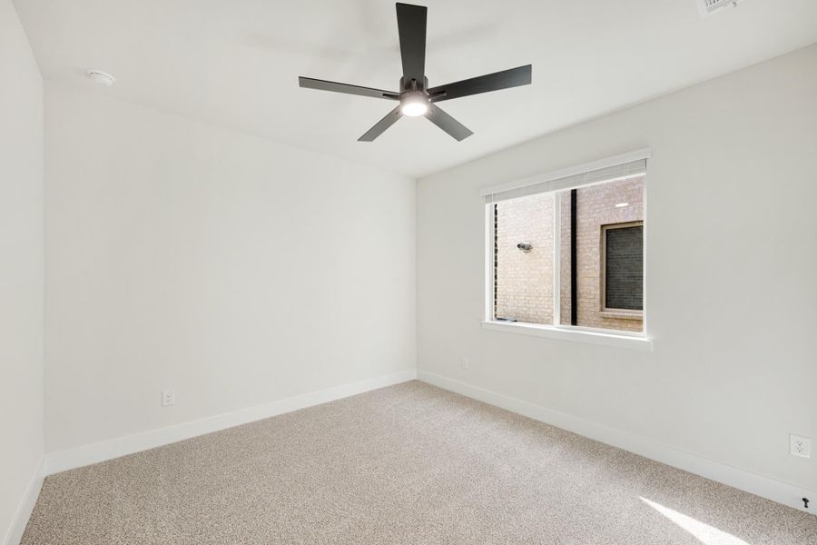 Empty bedroom with white walls, beige carpet, black ceiling fan, and single window