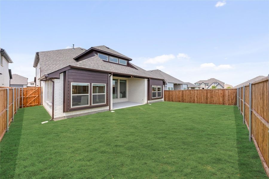 Rear exterior of home with brick and dark siding, covered patio, large grassy backyard, and wood privacy fence.