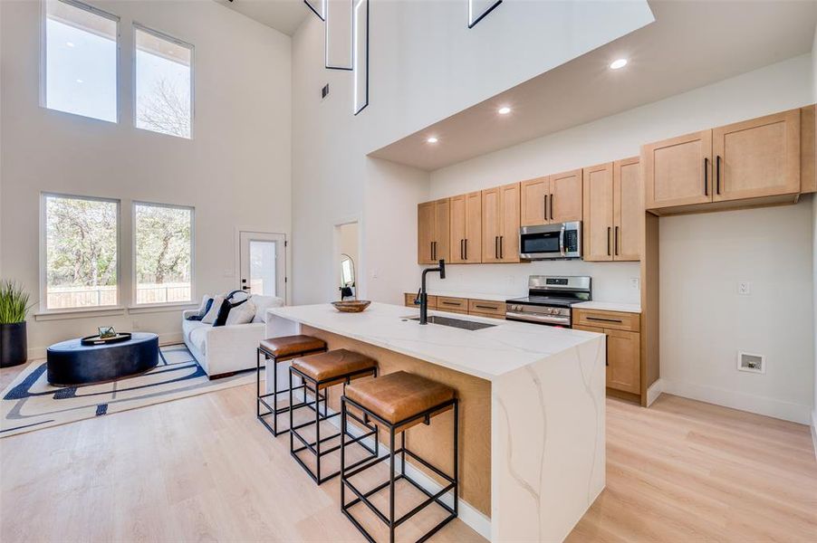 Kitchen featuring stainless steel appliances, sink, a high ceiling, light hardwood / wood-style floors, and an island with sink