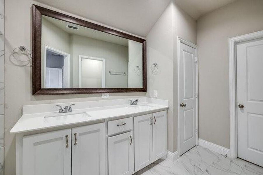 Full bath with double vanity, marble finish flooring, and baseboards