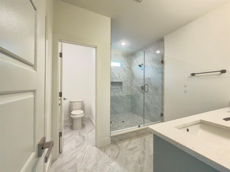 Contemporary bathroom featuring a glass-enclosed shower with pebble-tile floor, recessed lighting, and a window