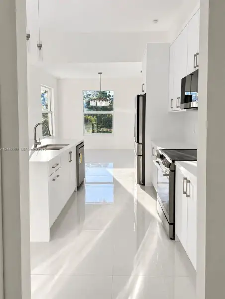 Kitchen featuring white cabinetry, solid-surface countertops, large-format tile flooring, stainless steel appliances, and a polished chrome kitchen faucet
