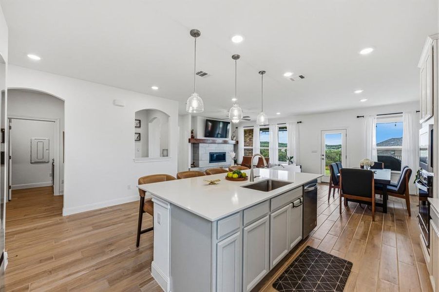 This open-concept living space features a kitchen island with seating, a dining area, and a living room with a stone fireplace