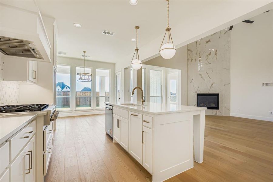 Kitchen with white cabinets, pendant lighting, a kitchen island with sink, a premium fireplace, and custom range hood
