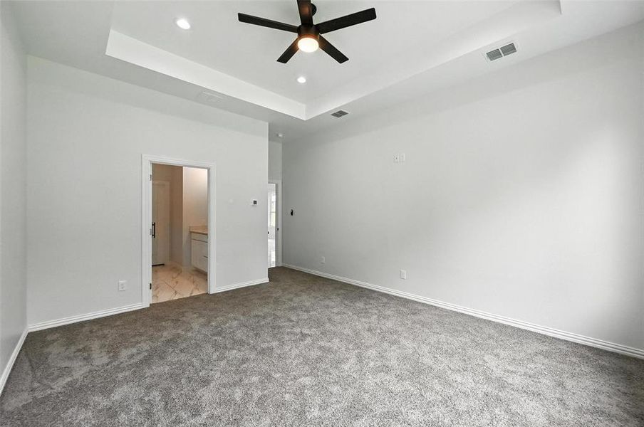 Unfurnished bedroom with a tray ceiling, light colored carpet, recessed lighting, ensuite bathroom, and ceiling fan