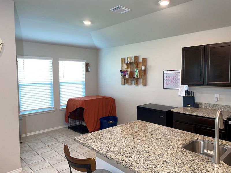 Kitchen featuring light stone countertops, light tile patterned flooring, a kitchen bar, lofted ceiling, and dark brown cabinets