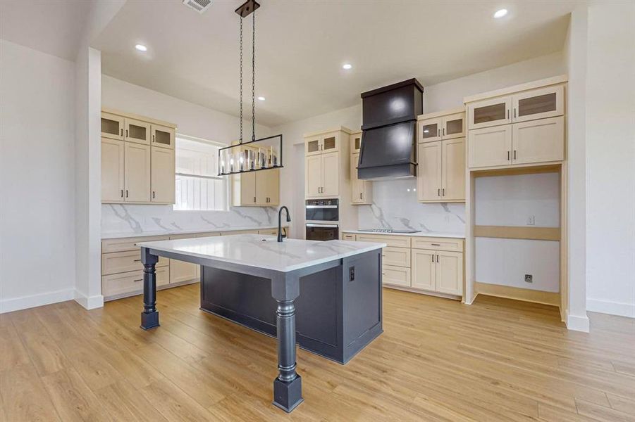 Kitchen featuring tasteful backsplash, an island with sink, light hardwood / wood-style floors, black appliances, and hanging light fixtures