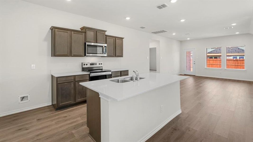 Kitchen featuring an island with a double basin sink, dark wood-finish cabinetry, stainless steel appliances, and light-toned countertops