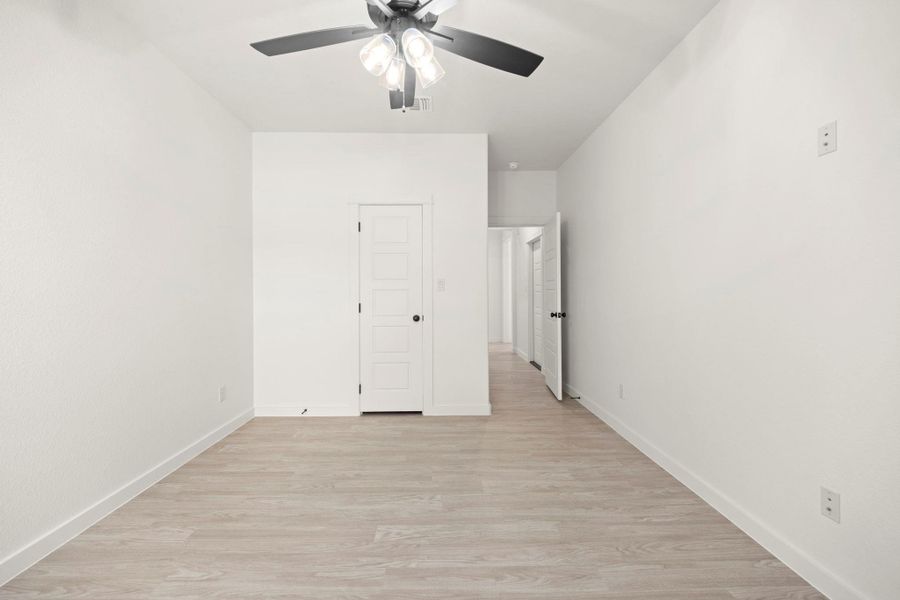 A quiet, neutrally finished bedroom with light wood flooring and a modern ceiling fan.
