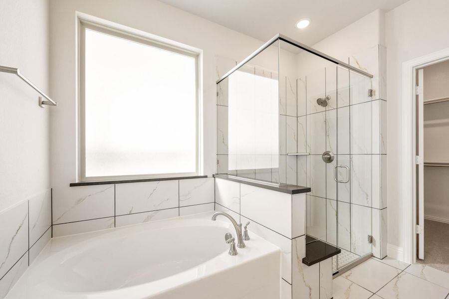 Master bathroom with soaking tub, glass walk-in shower, marble tile walls, and walk-in closet access Master bathroom with soaking tub, glass walk-in shower, marble tile walls, and walk-in closet access