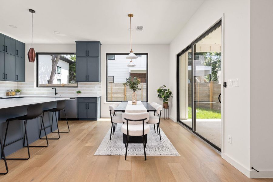 An open-concept living space features a sleek kitchen island and a dining area, with abundant natural light from large windows and sliding glass doors.