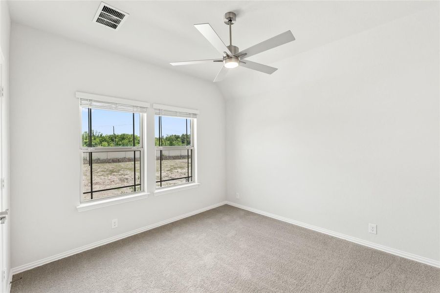 Empty bedroom with vaulted ceiling, ceiling fan, carpet flooring, and two windows with backyard view Empty bedroom with vaulted ceiling, ceiling fan, carpet flooring, and two windows with backyard view