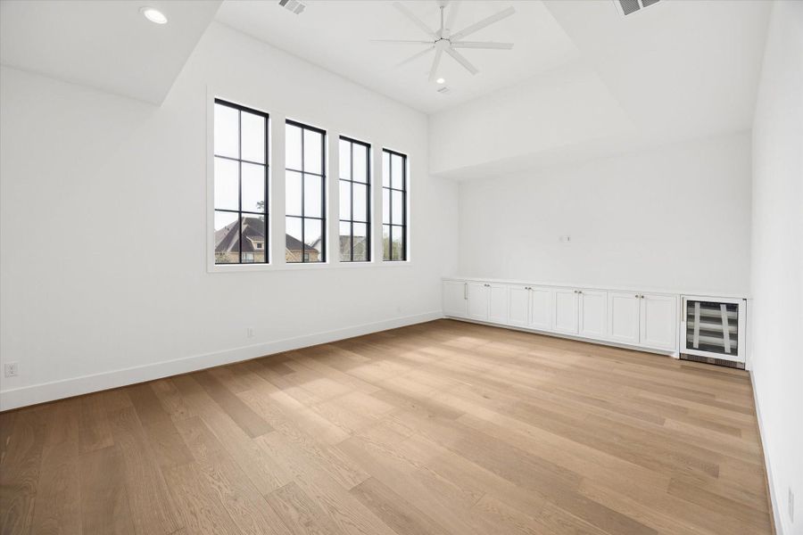 Vaulted ceilings and wide plank hardwood floors define this upstairs game room filled with natural light from oversized black framed windows. Custom built in cabinetry with a beverage fridge adds convenience, creating a flexible media or lounge space designed for entertaining and everyday living.
