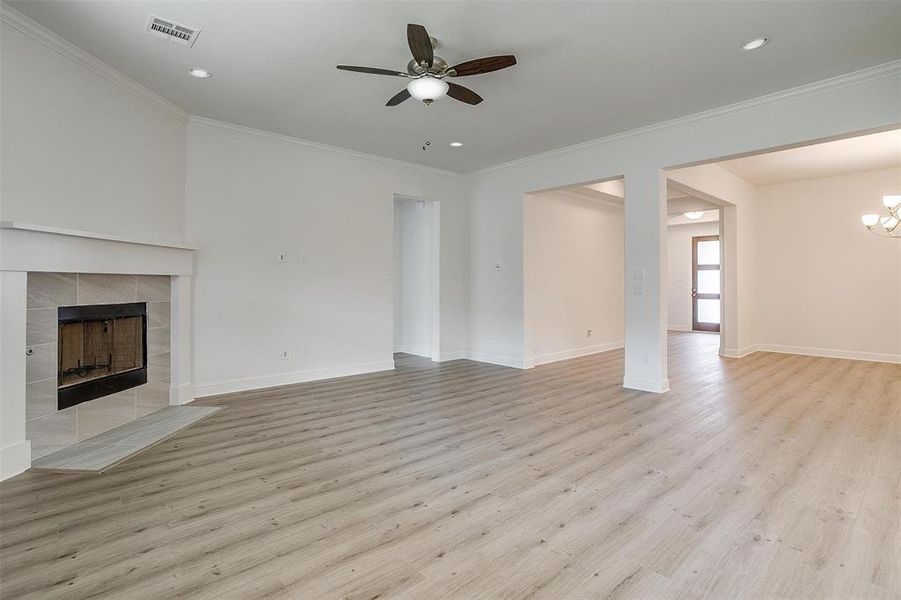 Unfurnished living room featuring a tiled fireplace, ornamental molding, ceiling fan, and light hardwood / wood-style floors