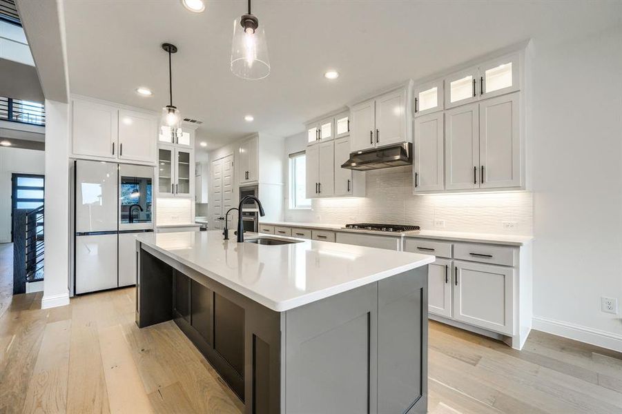 Kitchen featuring light wood-type flooring, under cabinet range hood, a sink, gas stovetop, and refrigerator with glass door