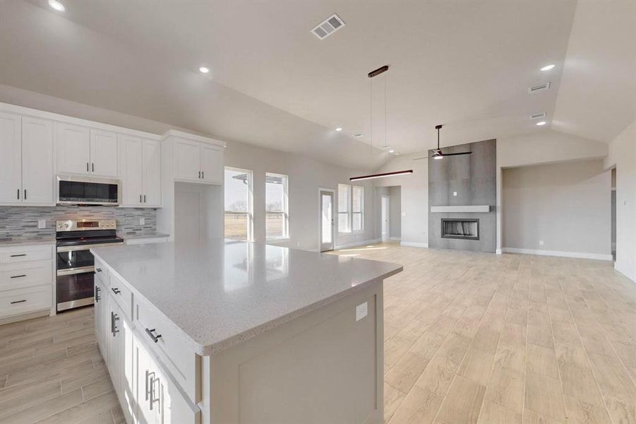 Kitchen with visible vents, backsplash, appliances with stainless steel finishes, a fireplace, and lofted ceiling