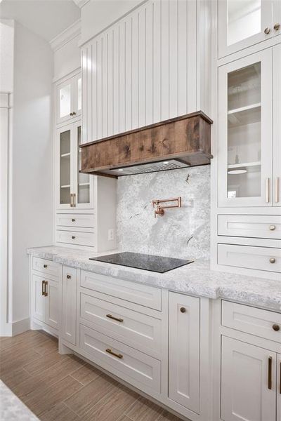 Kitchen featuring white cabinetry, glass insert cabinets, tasteful backsplash, custom range hood, and light stone countertops