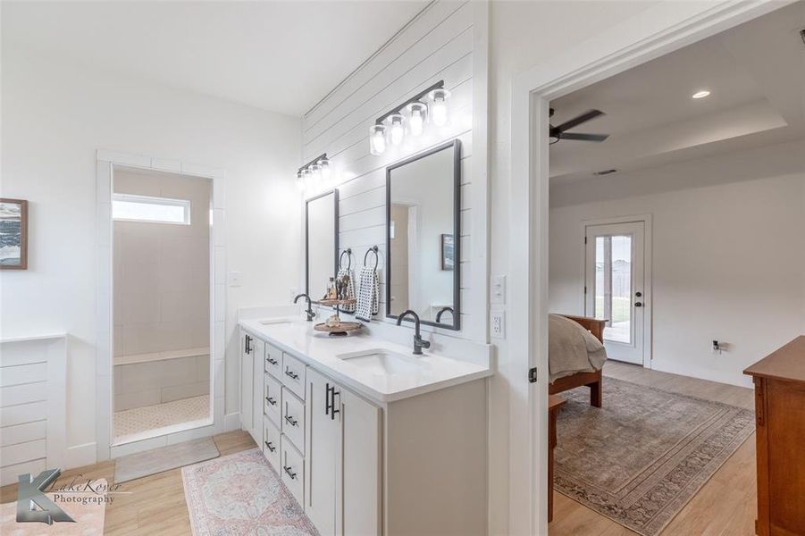 Bathroom featuring light wood-style floors, double vanity, walk in shower, ceiling fan, and ensuite bath Bathroom featuring light wood-style floors, double vanity, walk in shower, ceiling fan, and ensuite bath