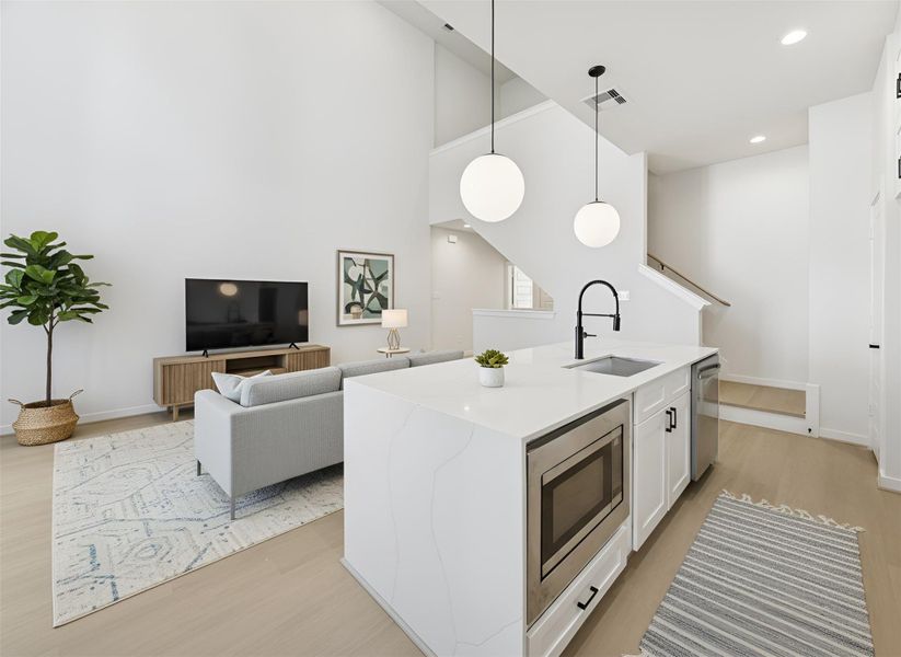 A further view from the balcony door showcases the kitchen’s waterfall-edge island and modern finishes, emphasizing the open-concept layout and soaring 20-ft ceilings that fill the space with light and airiness. *Virtually staged*