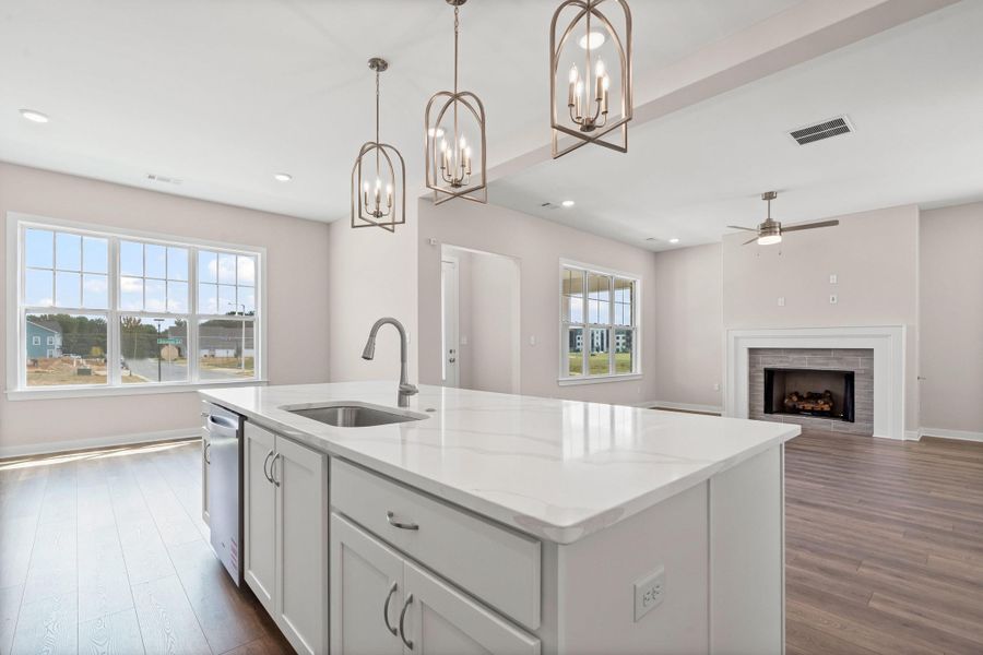 Kitchen featuring white cabinets, decorative light fixtures, a center island with sink, light stone counters, and open floor plan