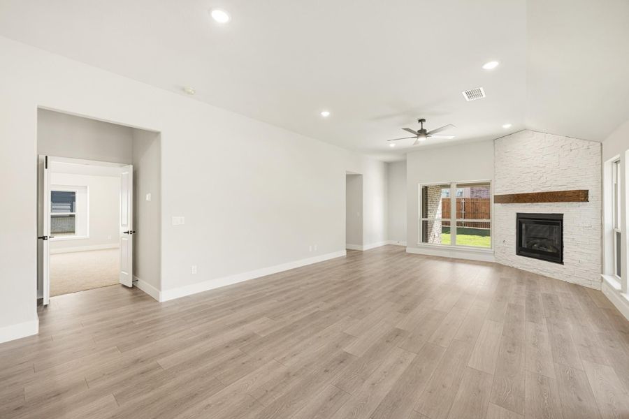 Open living room with light wood floors, white stone fireplace, and ceiling fan Open living room with light wood floors, white stone fireplace, and ceiling fan