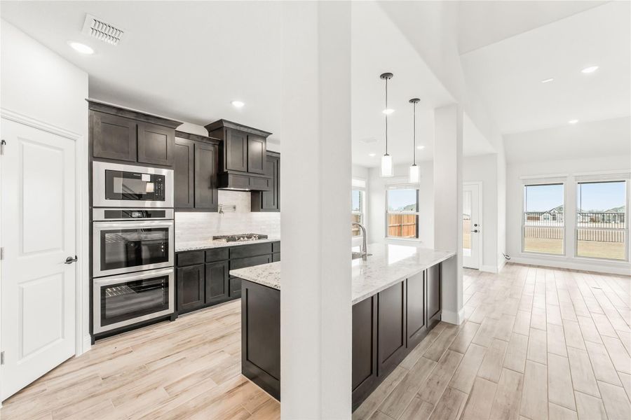 Kitchen with dark cabinets, stainless steel appliances, granite island, and light wood floors open to living area Kitchen with dark cabinets, stainless steel appliances, granite island, and light wood floors open to living area