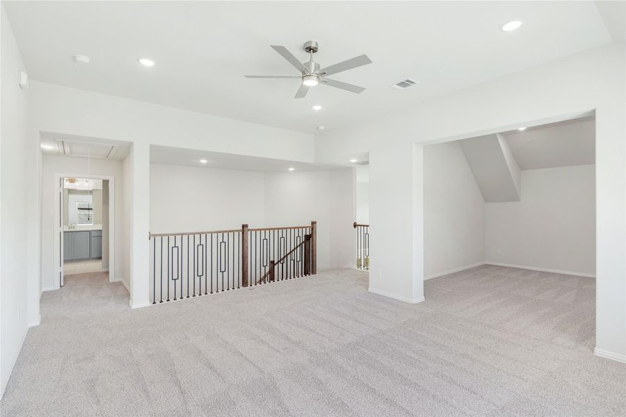Spacious upstairs loft with gray carpet, ceiling fan, and open staircase railing