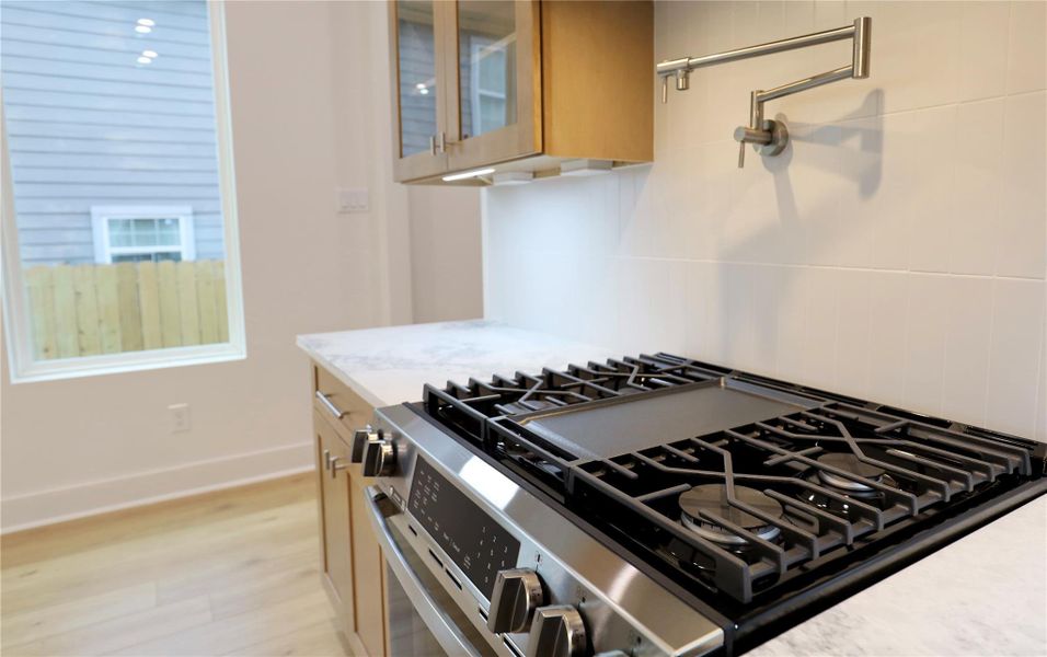 The gas range with a built-in griddle and overhead pot filler anchors this stylish, chef-ready kitchen. Notice the uninterrupted backsplash, the outlets are hidden beneath the cabinetry. The gas range with a built-in griddle and overhead pot filler anchors this stylish, chef-ready kitchen. Notice the uninterrupted backsplash, the outlets are hidden beneath the cabinetry.