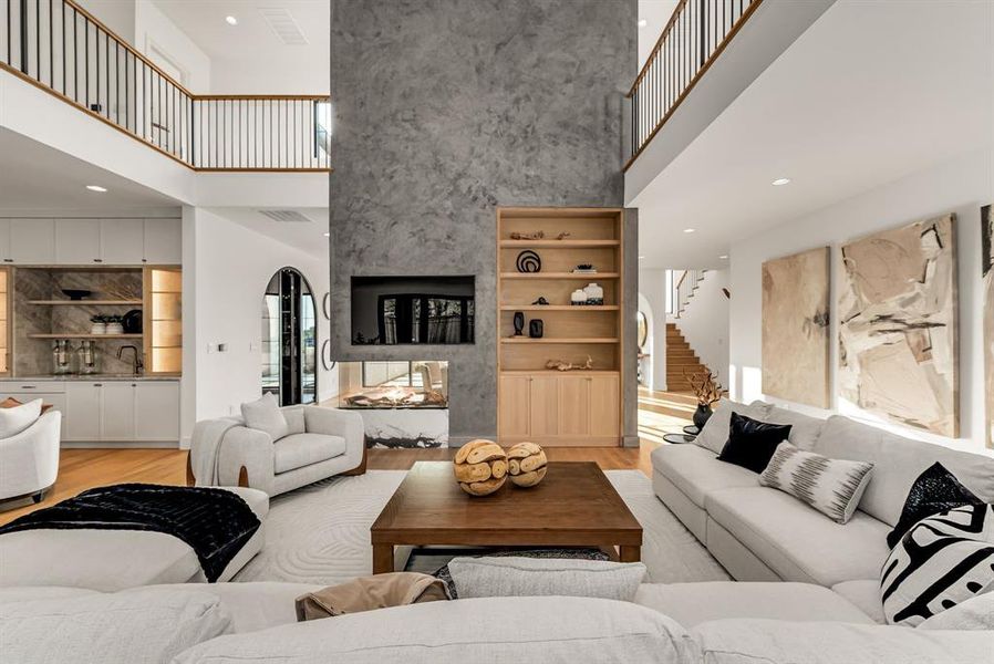 Living area featuring recessed lighting, light wood-type flooring, a towering ceiling, stairway, and a fireplace Living area featuring recessed lighting, light wood-type flooring, a towering ceiling, stairway, and a fireplace