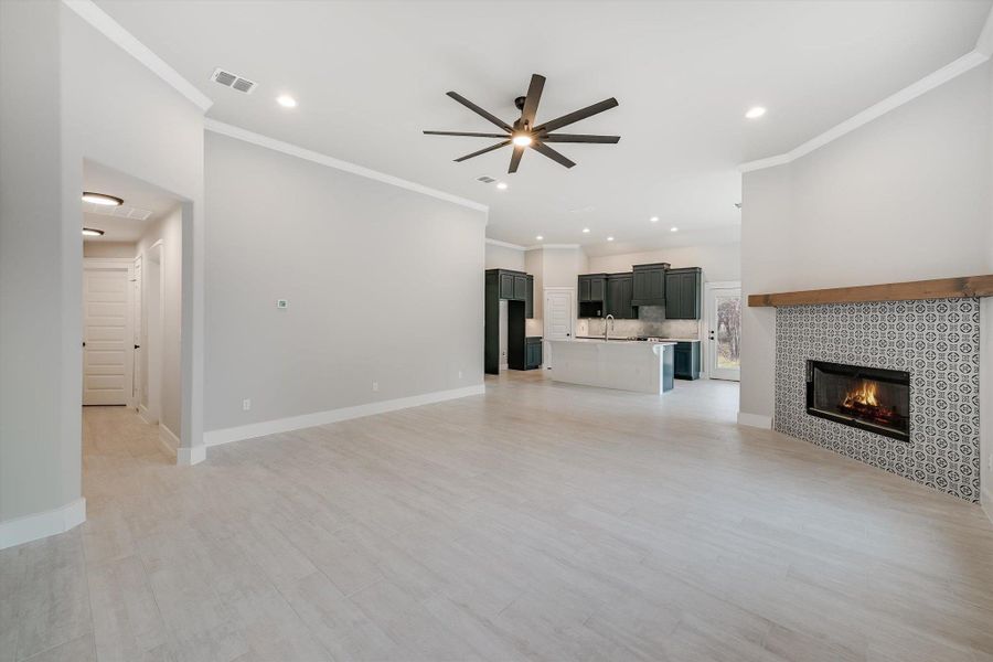 Unfurnished living room featuring a sink, visible vents, a ceiling fan, baseboards, and a tiled fireplace