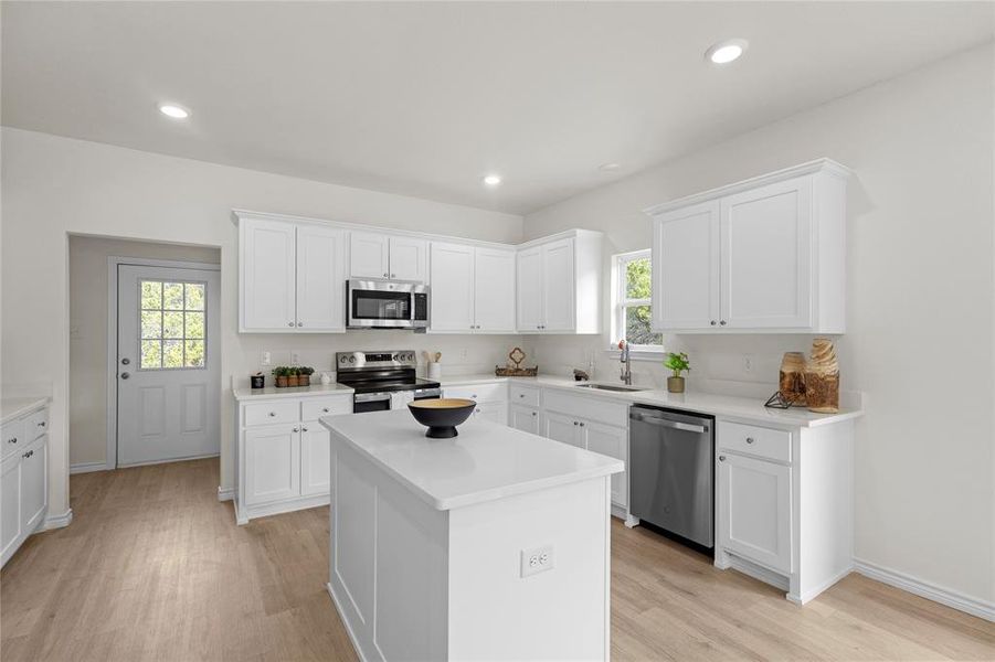 Kitchen featuring white cabinetry, stainless steel appliances, light wood-style floors, a kitchen island, and recessed lighting Kitchen featuring white cabinetry, stainless steel appliances, light wood-style floors, a kitchen island, and recessed lighting