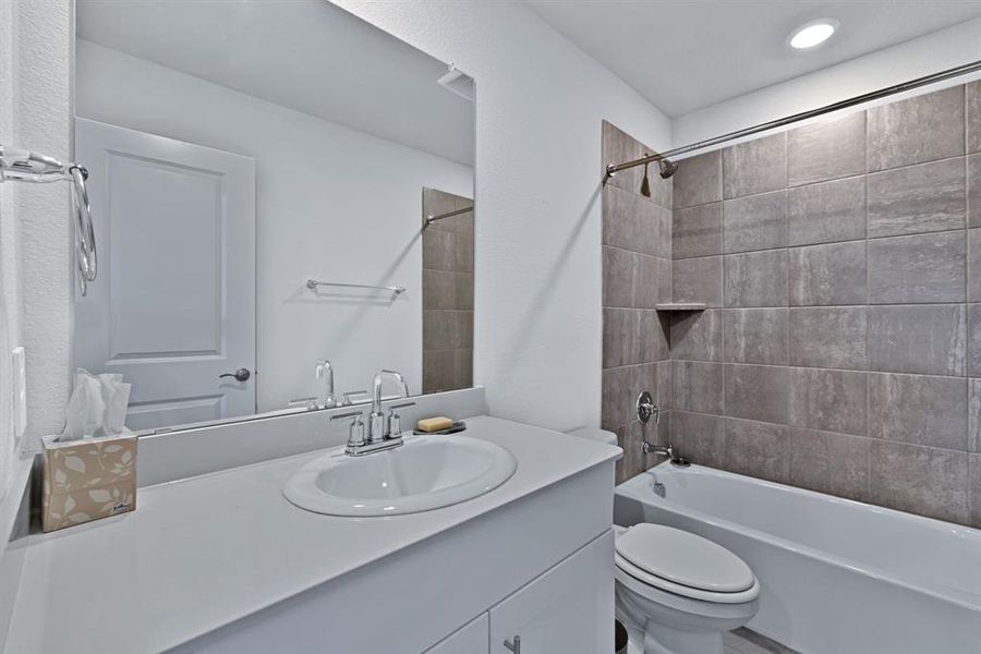 Bathroom featuring a vanity with an integrated sink, a large mirror, and a bathtub with tiled walls