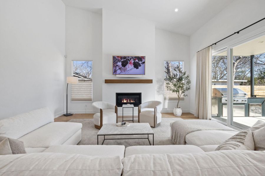 Living room with a glass covered fireplace, light wood-style floors, and a high ceiling