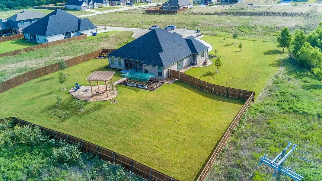 Spacious backyard featuring a wood pergola over a circular stone patio, raised garden beds, and a full privacy fence