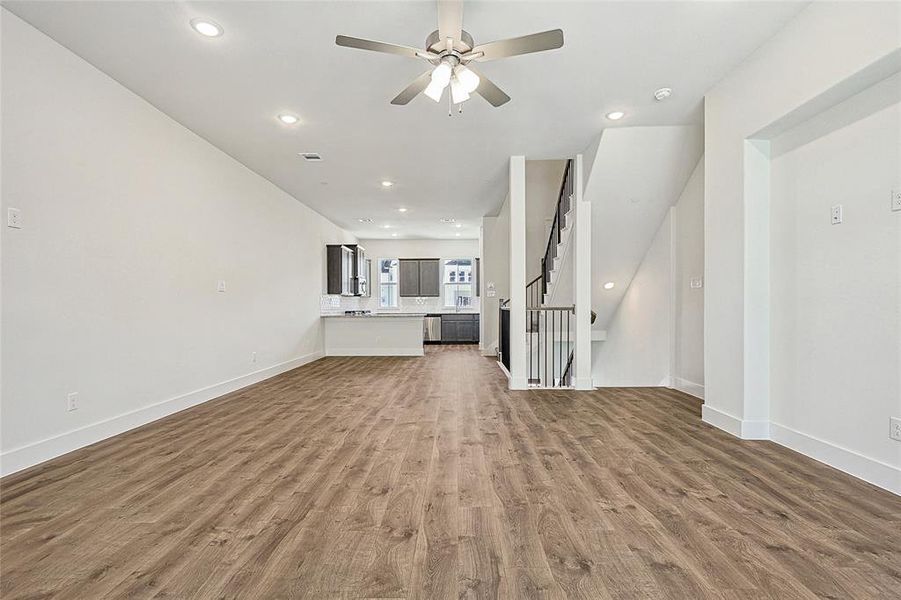 Unfurnished living room featuring dark wood finished floors, ceiling fan, recessed lighting, and stairs