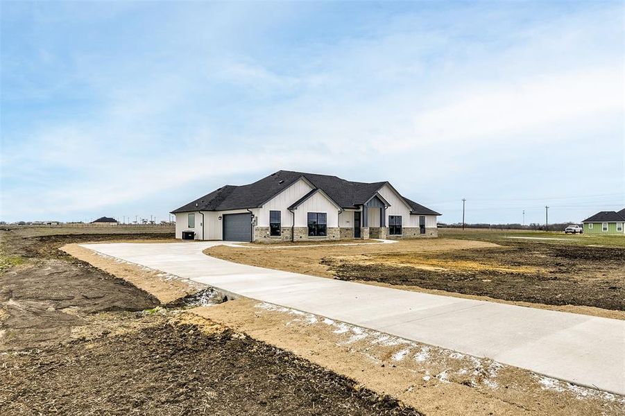 Modern farmhouse style home with driveway, a shingled roof, an attached garage, board and batten siding, and brick siding