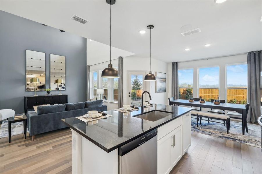 Kitchen featuring sink, dishwasher, hanging light fixtures, white cabinets, and a center island with sink