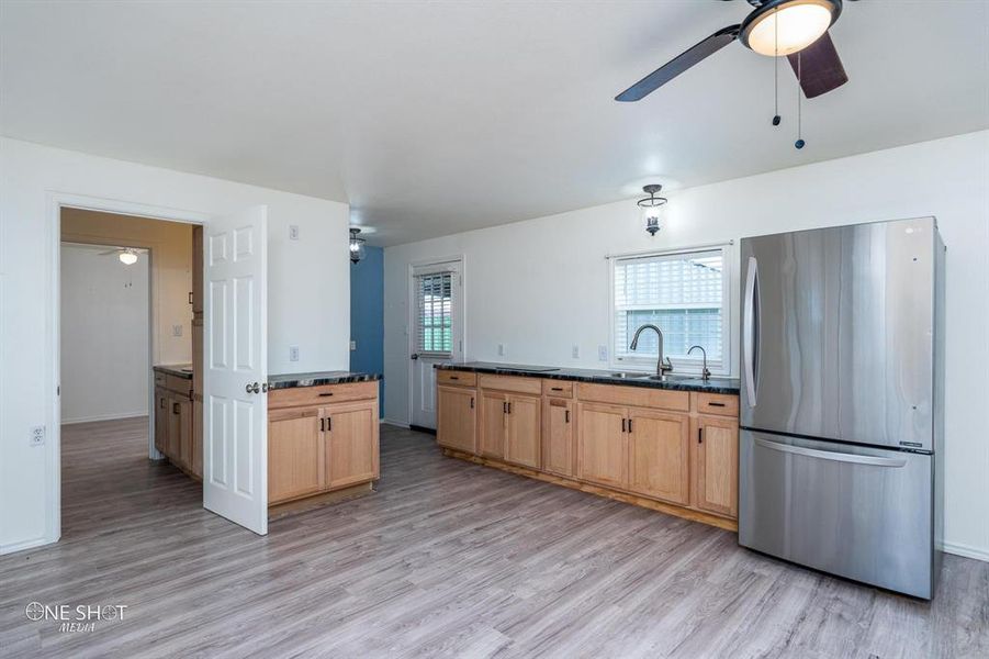 Kitchen with light hardwood / wood-style flooring, dark stone counters, ceiling fan, stainless steel fridge, and sink