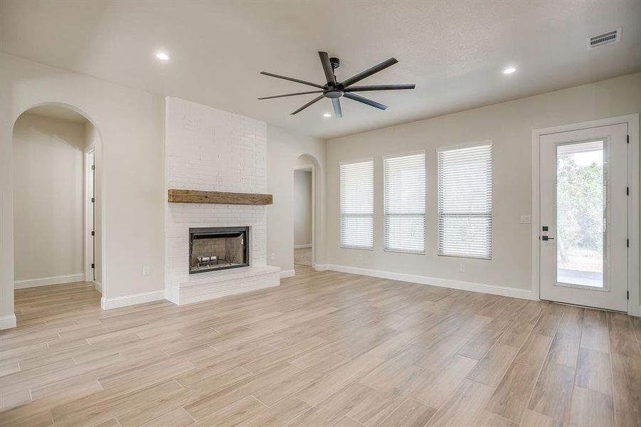 Unfurnished living room with light wood finished floors, arched walkways, a brick fireplace, ceiling fan, and recessed lighting Unfurnished living room with light wood finished floors, arched walkways, a brick fireplace, ceiling fan, and recessed lighting