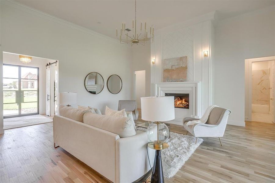 Living room featuring ornamental molding, light wood-type flooring, a chandelier, and a high ceiling