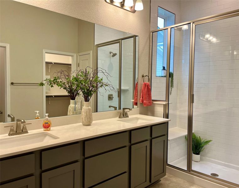 Full bath featuring a shower stall, double vanity, a spacious closet, and a textured wall Full bath featuring a shower stall, double vanity, a spacious closet, and a textured wall
