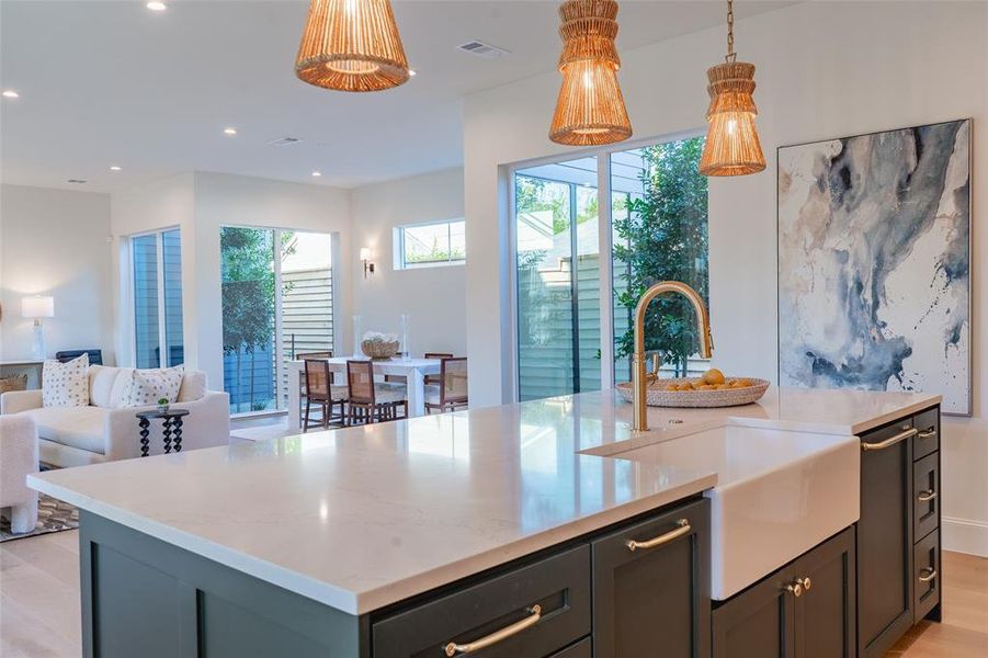 Kitchen featuring sink, light wood-type flooring, an island with sink, pendant lighting, and light stone counters