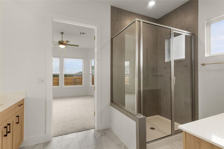 Bathroom featuring vanity, a shower stall, a ceiling fan, and marble look tiles