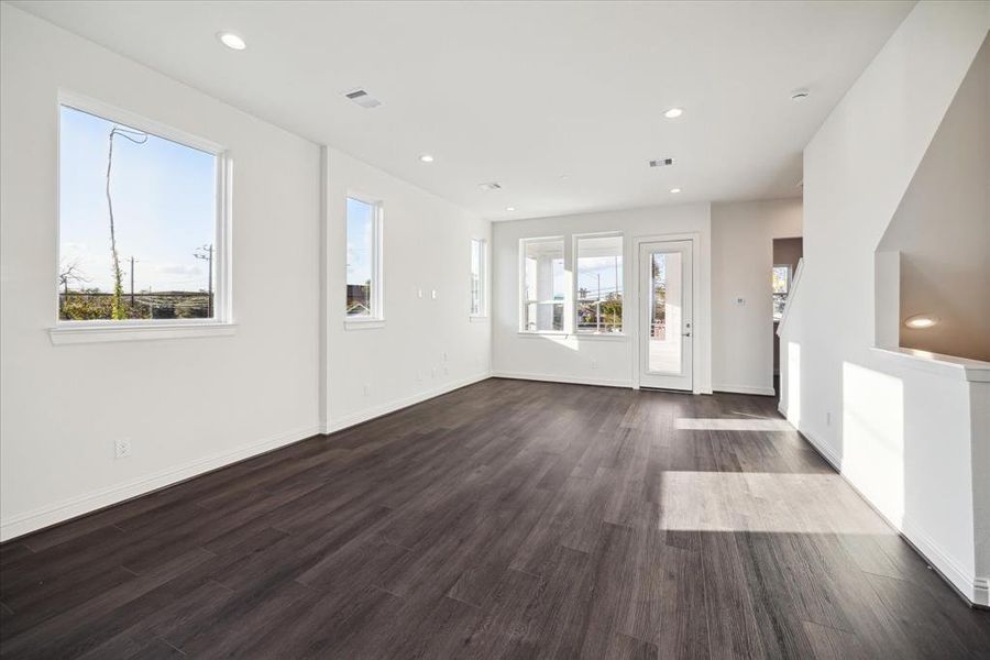 Flooded with natural light, this expansive living room features large windows and a glass door that seamlessly connects to the outdoors. The sleek dark wood flooring adds a touch of warmth and elegance, while the neutral palette provides the perfect backdrop for your personal style. With plenty of space for entertaining or relaxing, this open-concept layout makes it easy to create a living area that feels both modern and inviting.